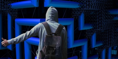 back of person in a grey hoodie, with a backpack, standing in a futuristic blue maze and holding out their thumb
