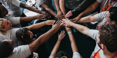 A group of 14 people in matching t-shirts, each extending one hand into the middle of their circle