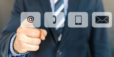 Man in suit pointing at one of four translucent symbols representing different methods of communication that are floating in front of him