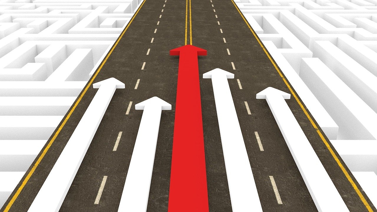 A red arrow leading four white arrows down a road, over a maze
