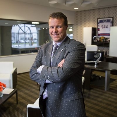 Aaron Zeigler standing in his office, wearing a gray suite, smiling, with his arms crossed