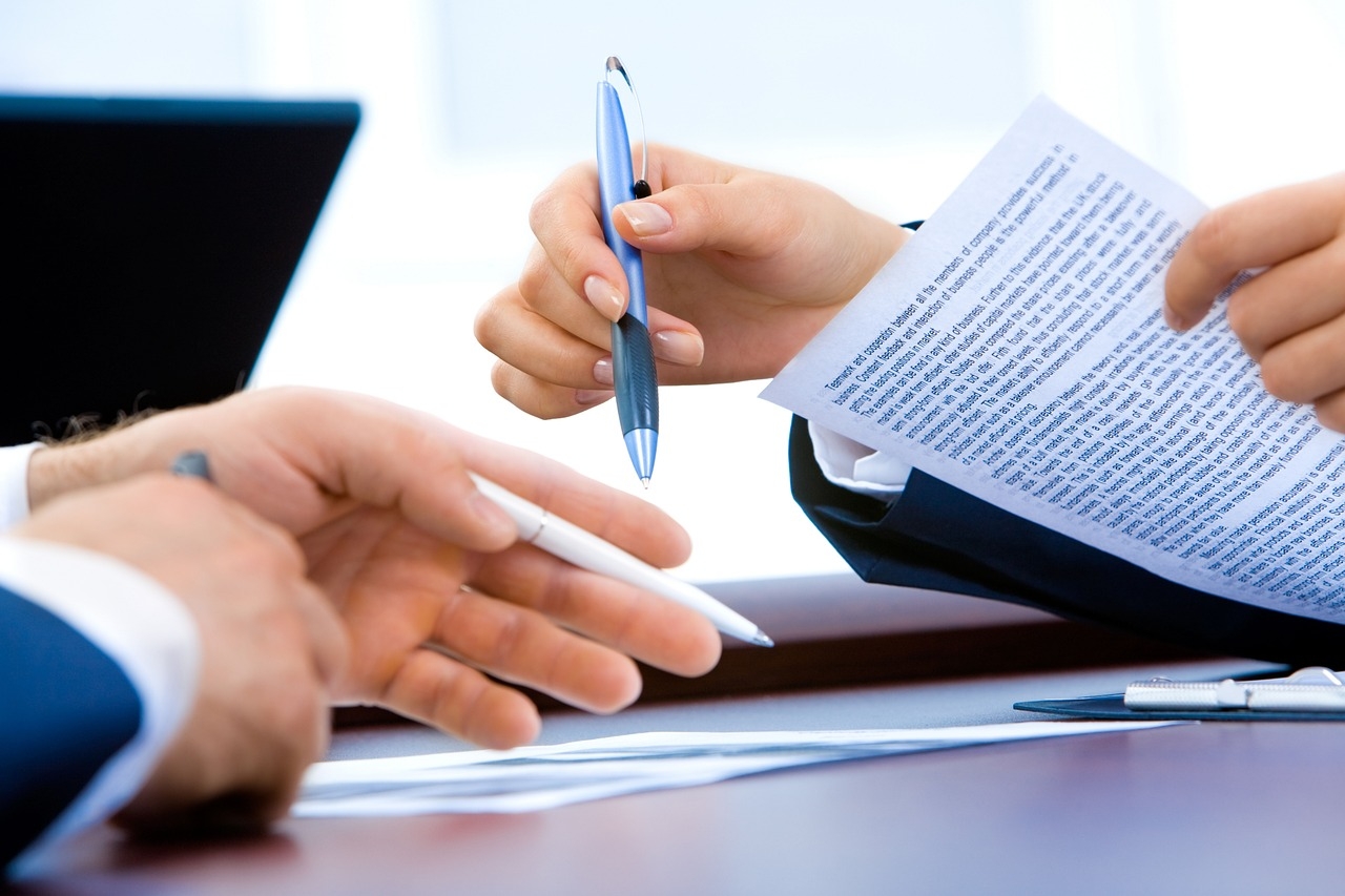 The hands of two men, sitting across from each other at a table, discussing a document