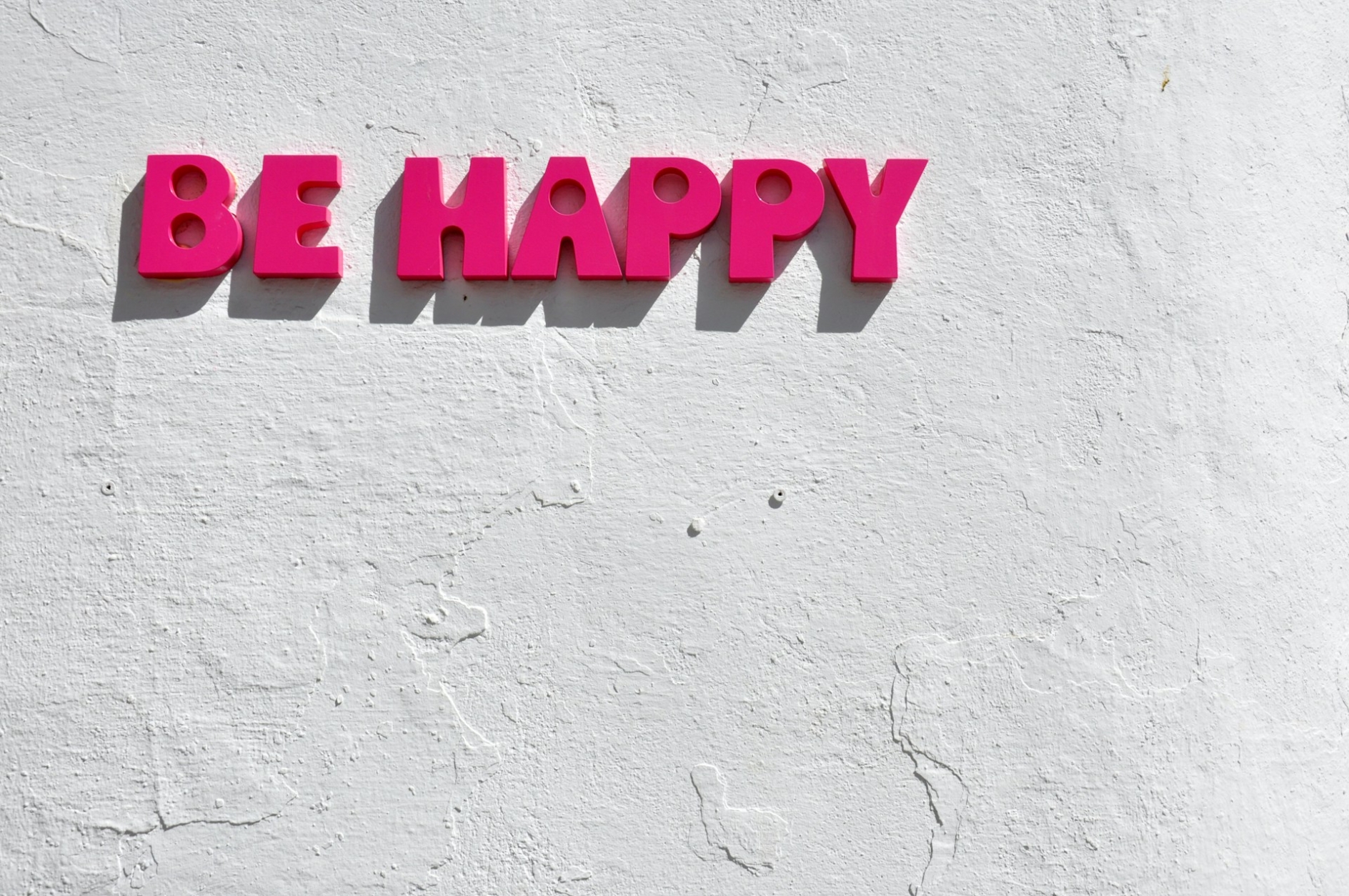 Magenta letters on a white wall that read "Be Happy"