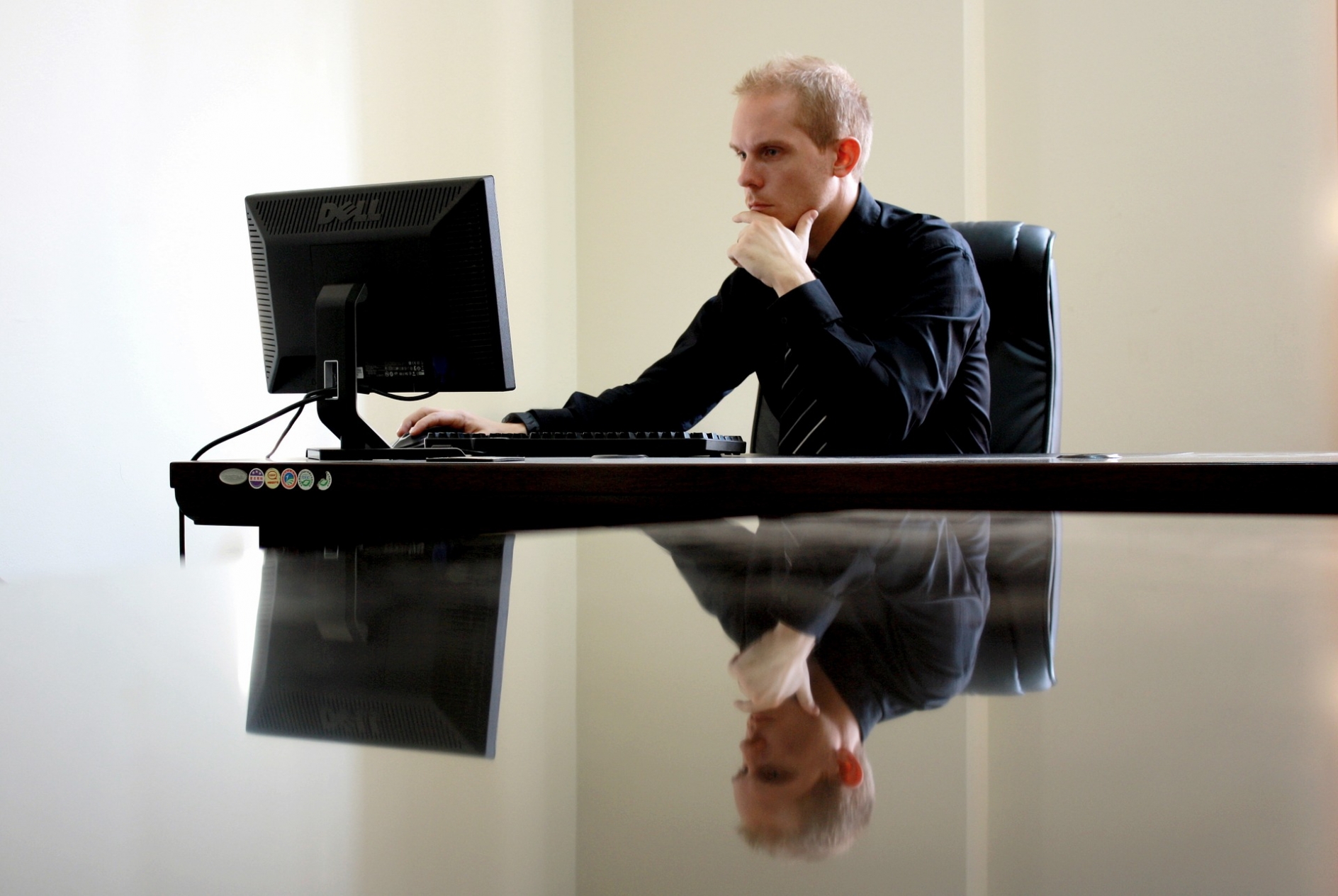 A white man sitting at a desk, looking intently at a computer screen and thinking