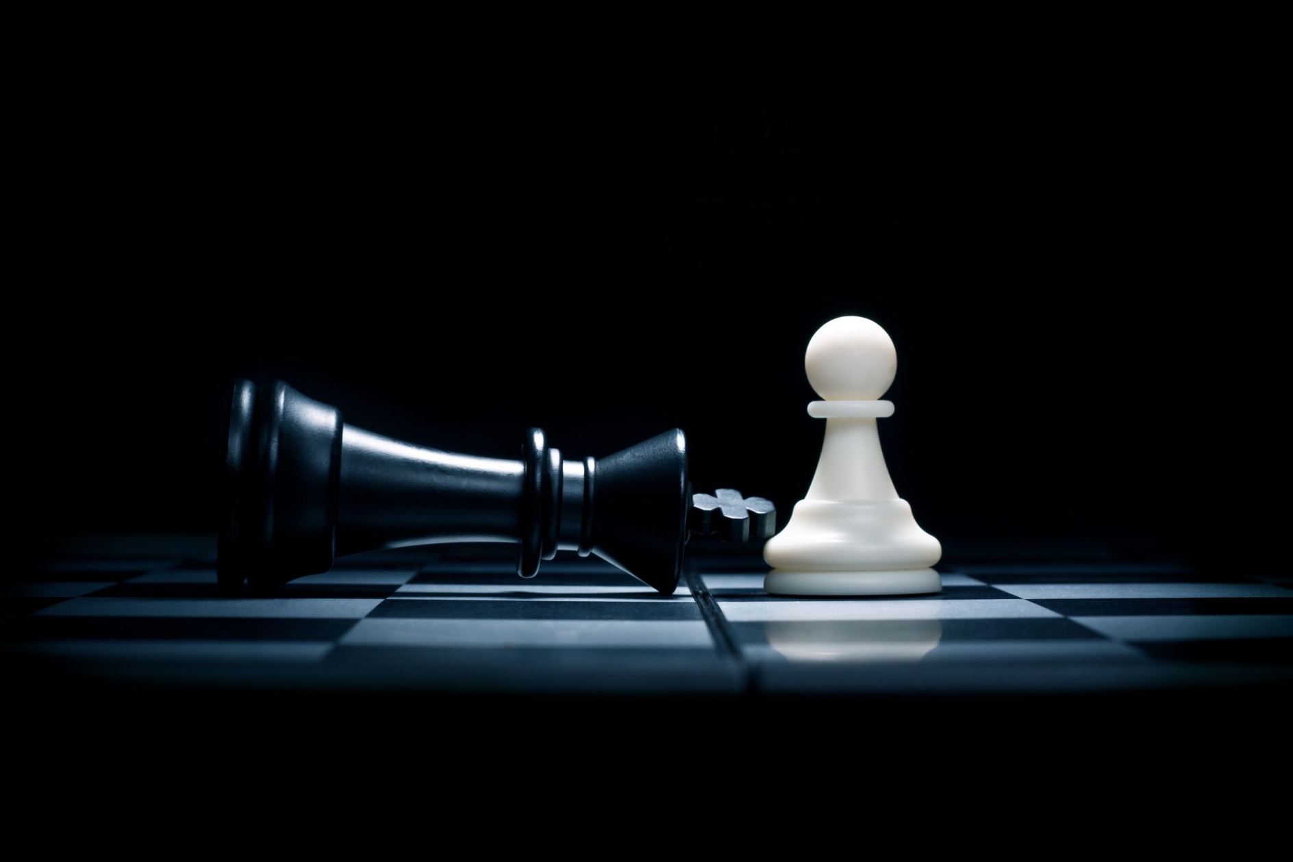 Chessboard with white pawn standing and black queen laying on it's side