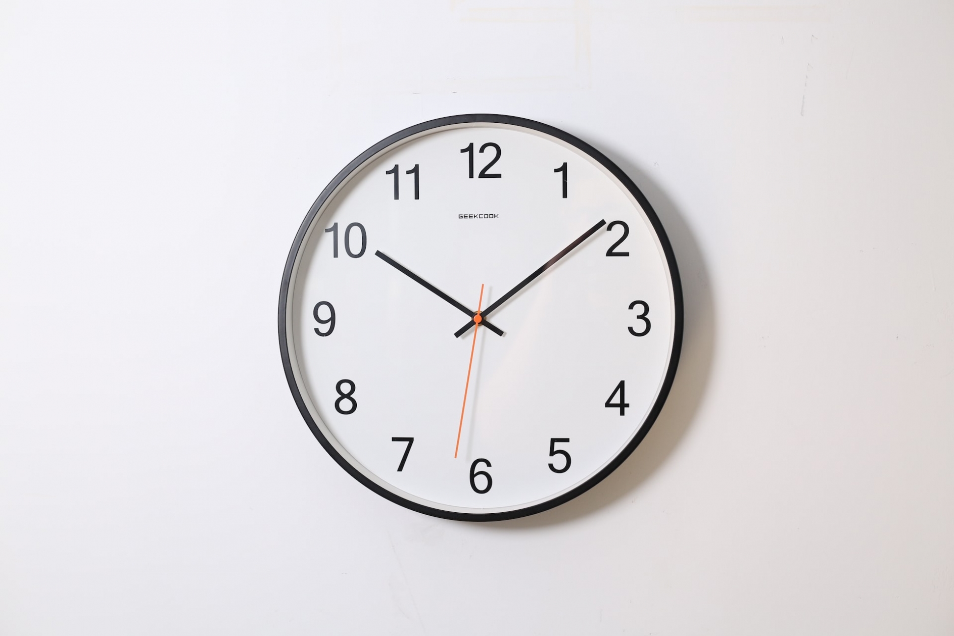 A large, round, analog clock, hanging on a blank wall, set to the time 10:09