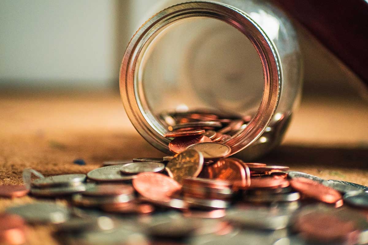 A glass jar on the floor with coins spilling out of it
