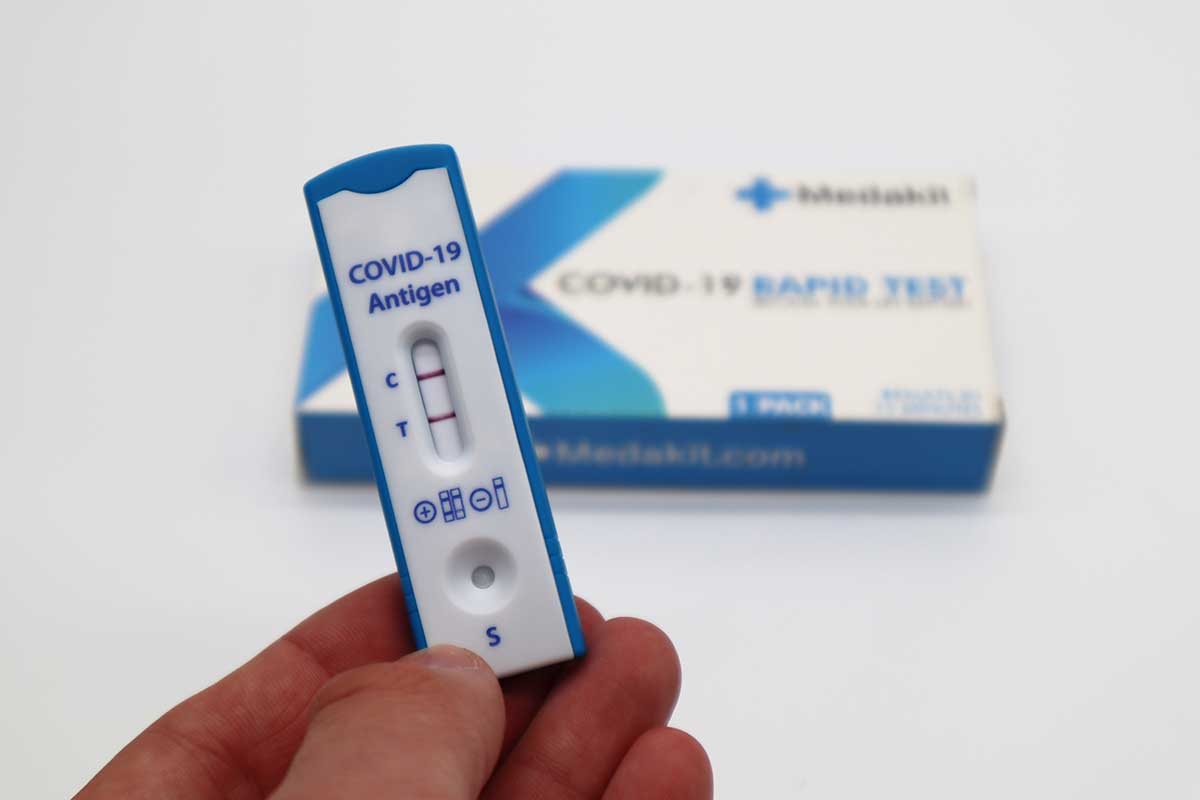 Fingers holding a blue and white COVID-19 antigen test showing a positive result