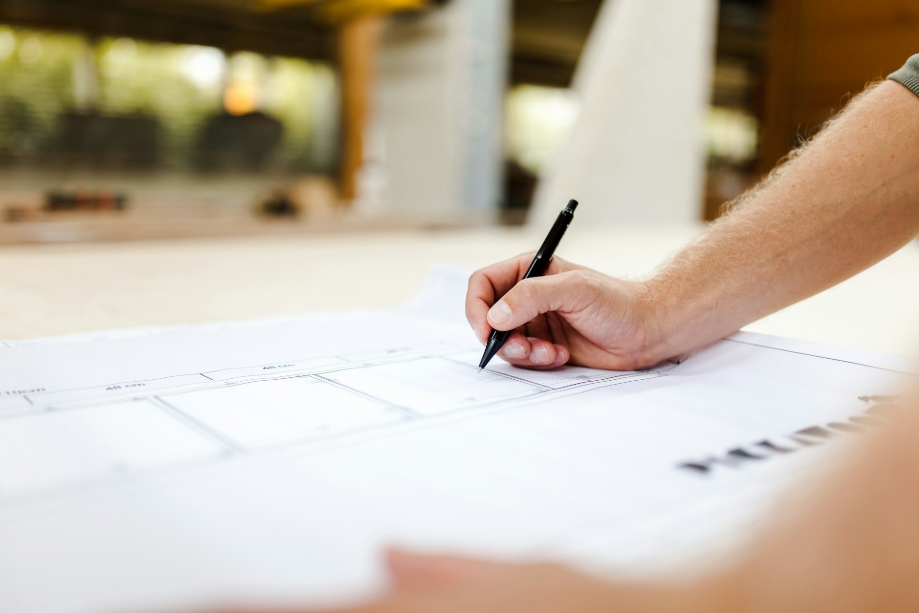 A hand, holding a pen, drawing on a blueprint