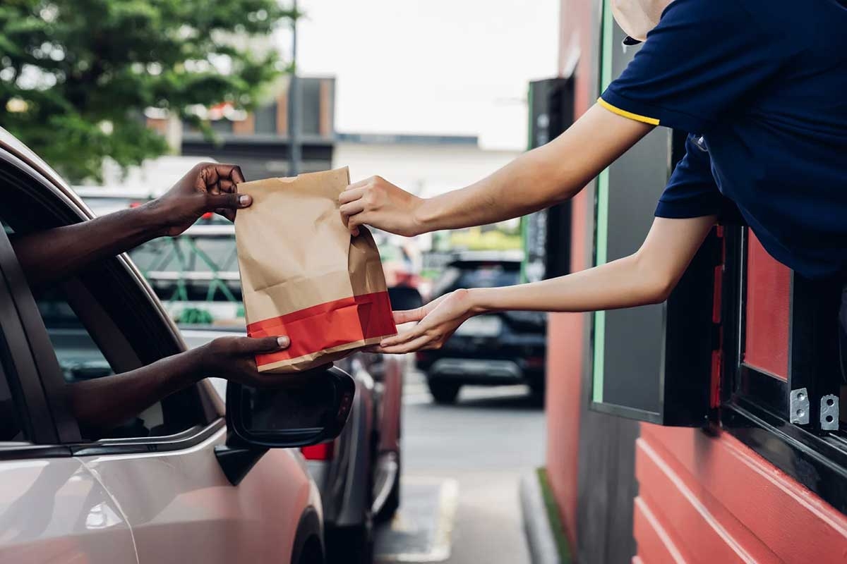 Hands reaching out a car window take a paper bag from someone reaching out a drive-through window