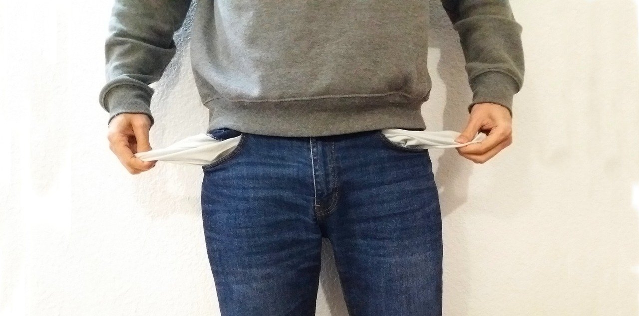 Man pulling the pockets out of his jeans to show they are empty