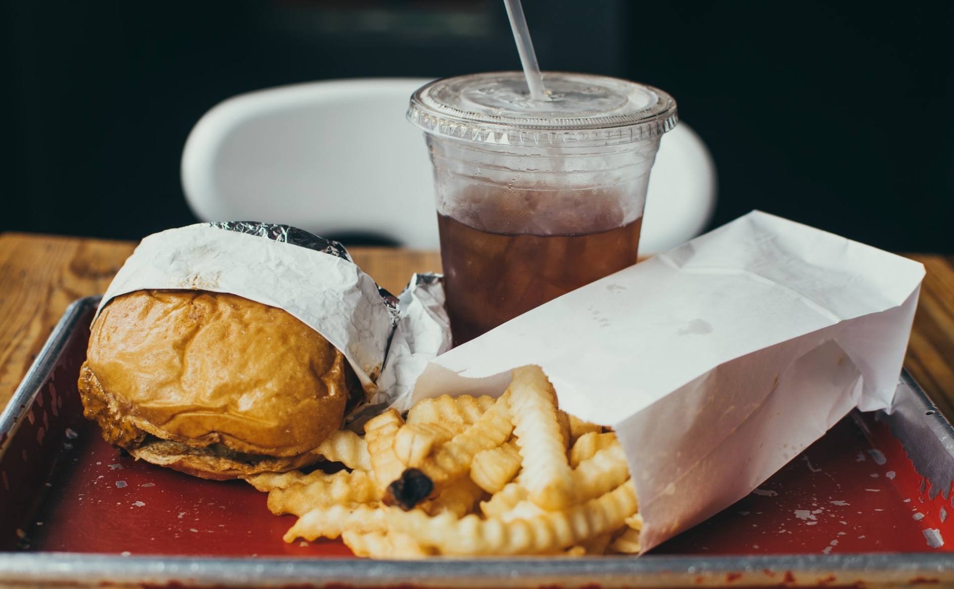 A hamburger, bag of french fries, and a soft drink in a plastic cup, all sitting on a desk