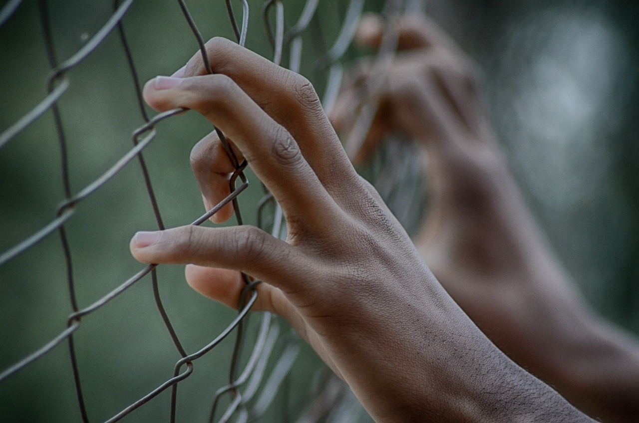 Photo of hands grasping a chain link fence