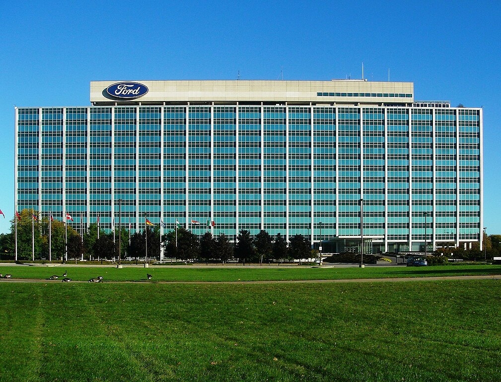 Large glass building with Ford emblem on top, next to a grass lawn
