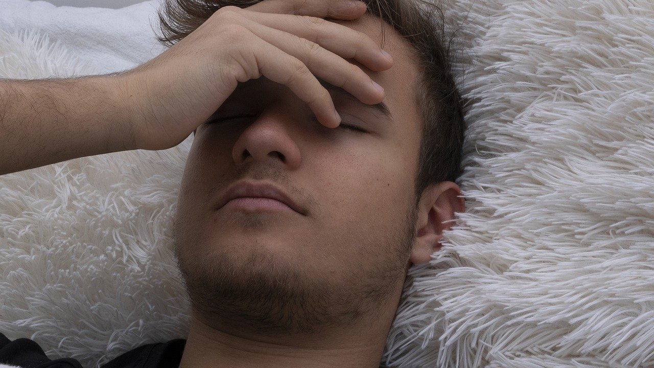 Young man laying on a furry white pillow with his hand on his face