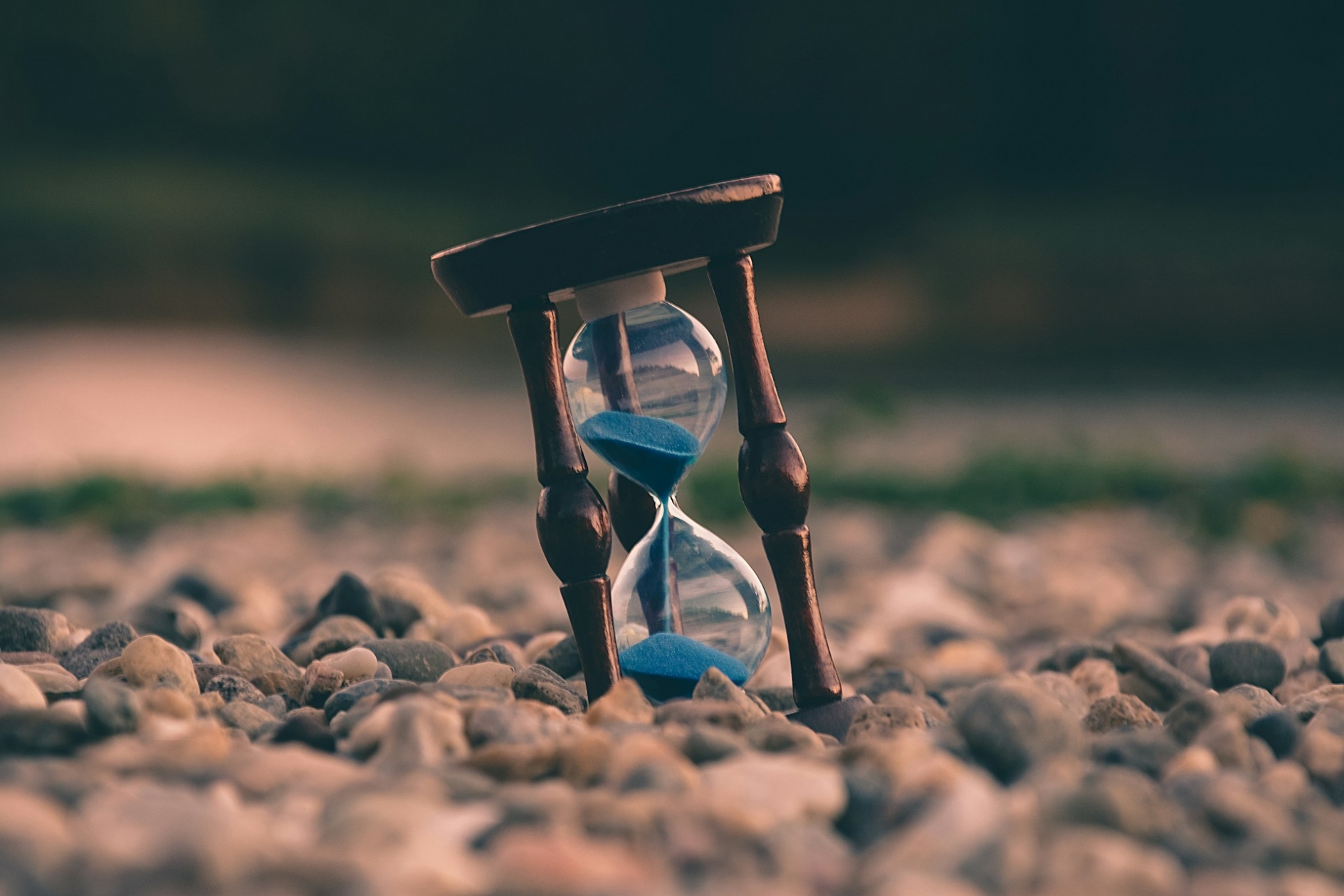 An hourglass with blue sand, sitting on a rocky surface