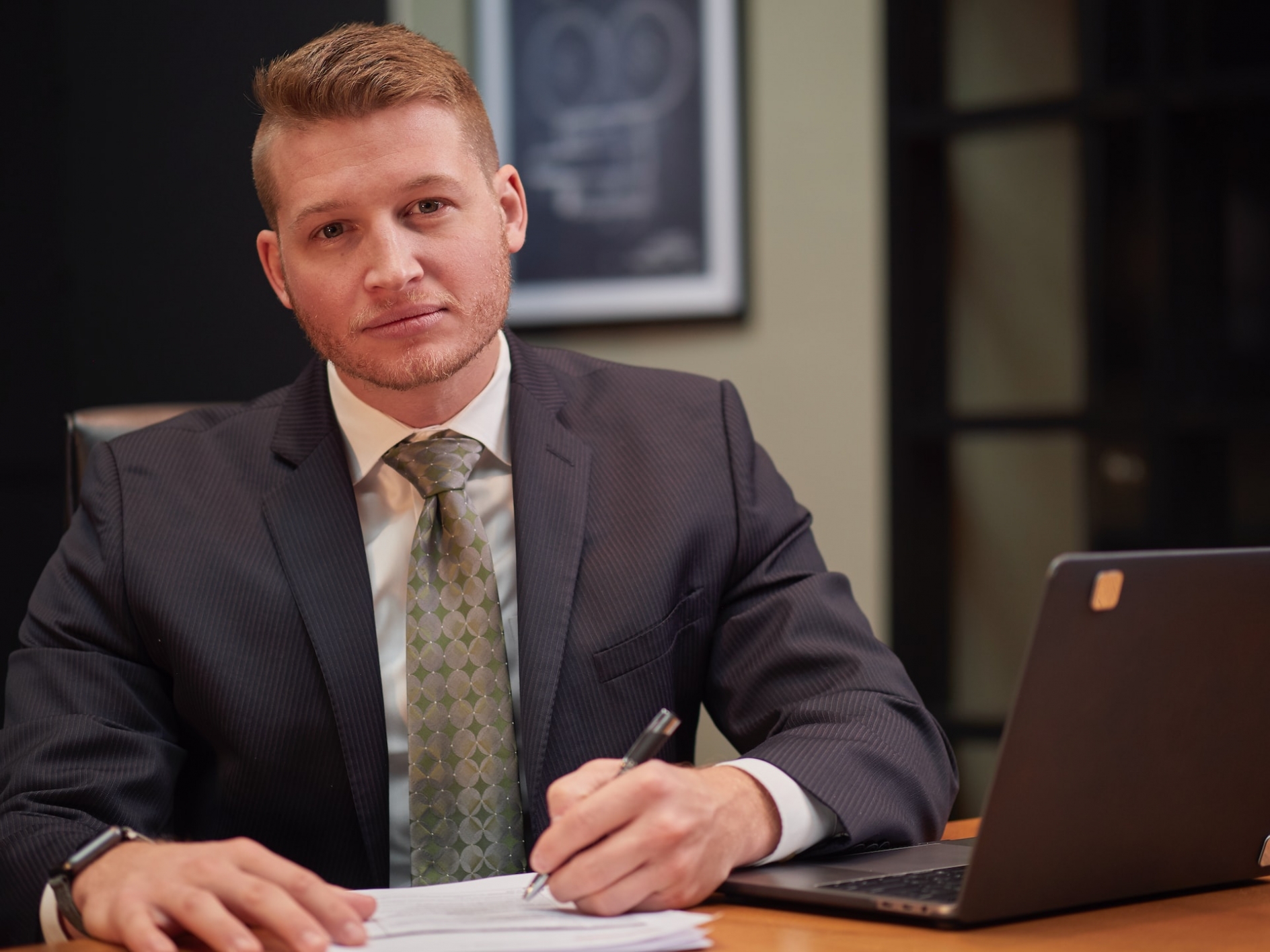 a man in a suit and tie, looking at the viewer while writing on a piece of paper