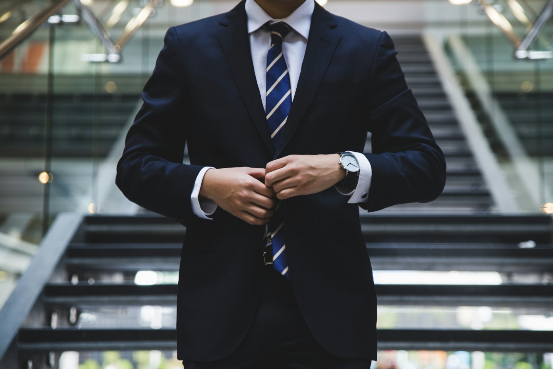 midsection of a man, wearing a suit and tie, buttoning his jacket