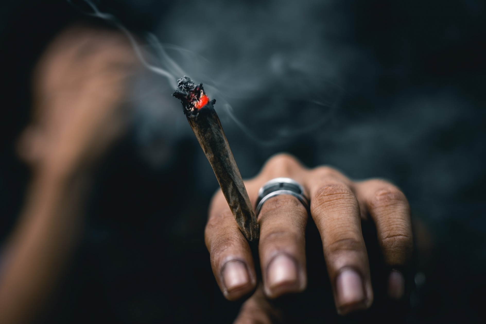 Man's hand holding a lit joint