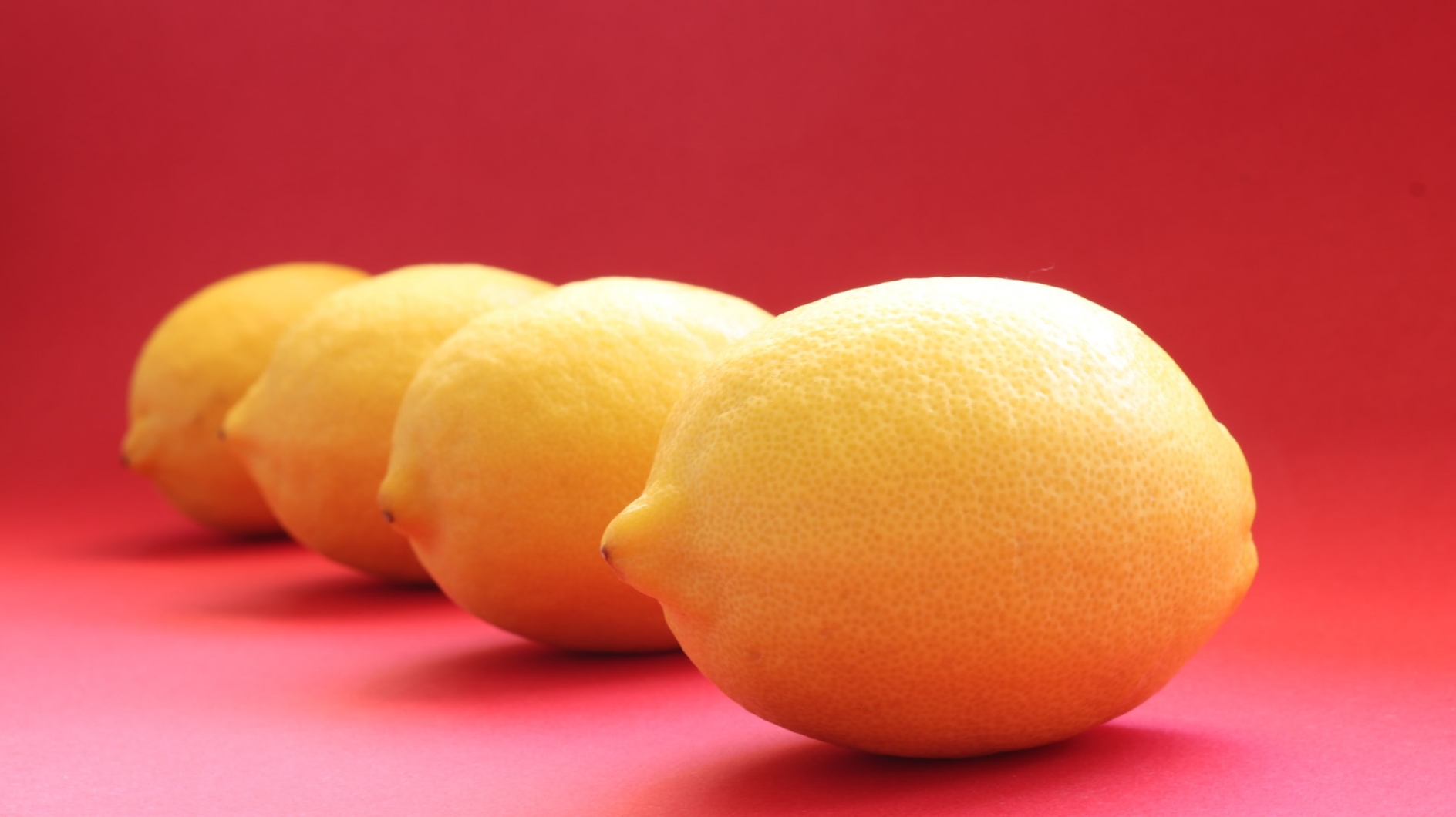 Four yellow lemons in a line, against a red background