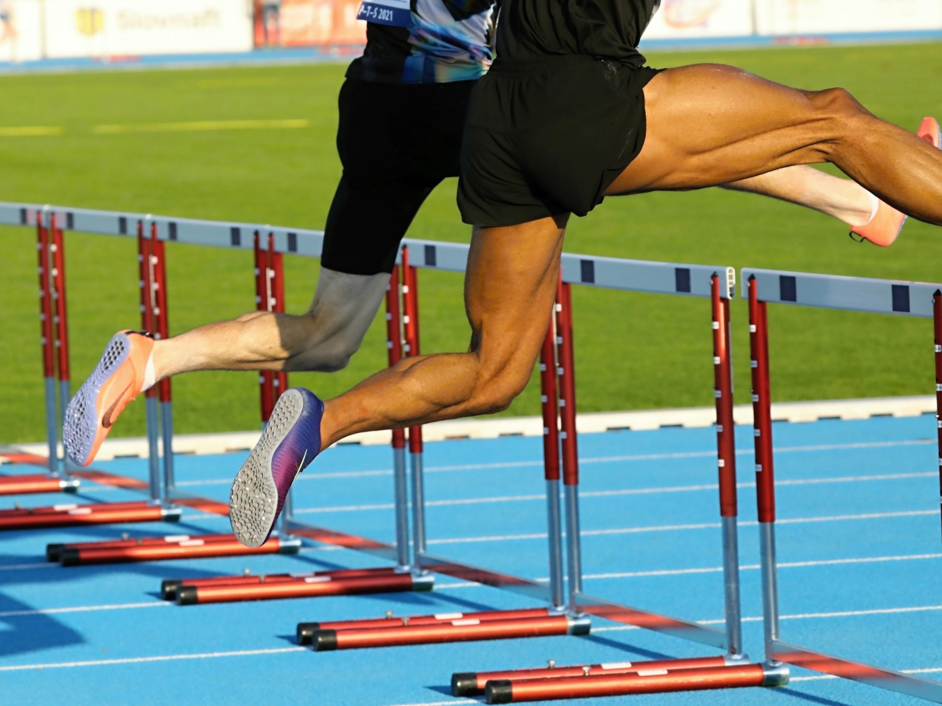 Two men photographed in mid jump over hurdles, while running neck and neck in a race