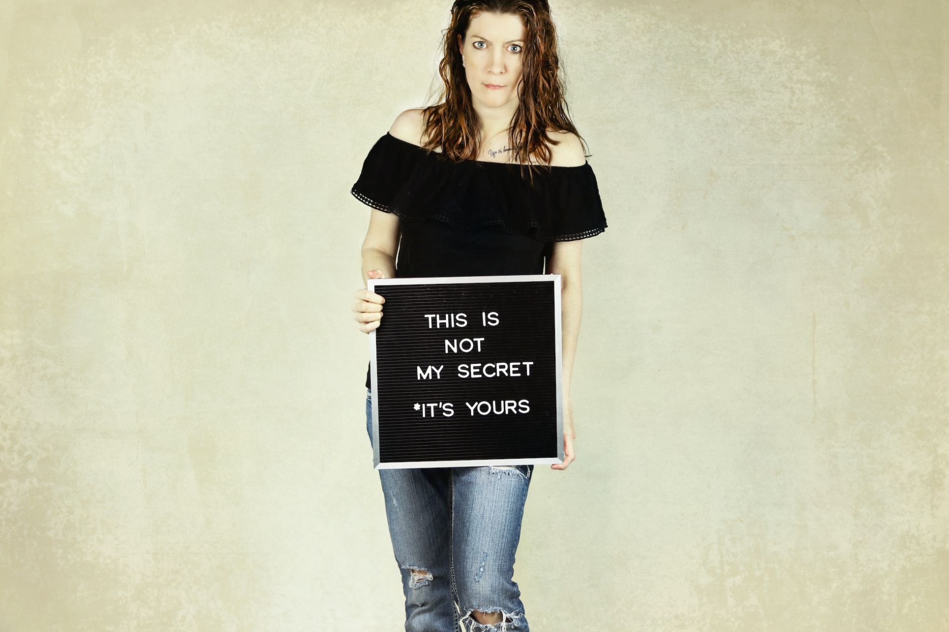 A woman holding a sign that reads: This is not my secret *It's yours