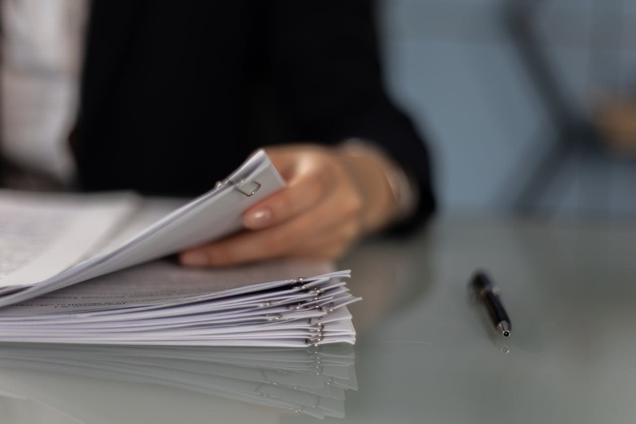 Close-up shot of a person holding a paperwork beside a pen