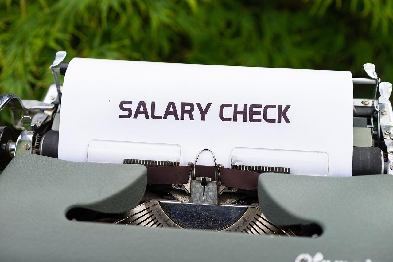 A typewriter holding a piece of paper with the words SALARY CHECK on it