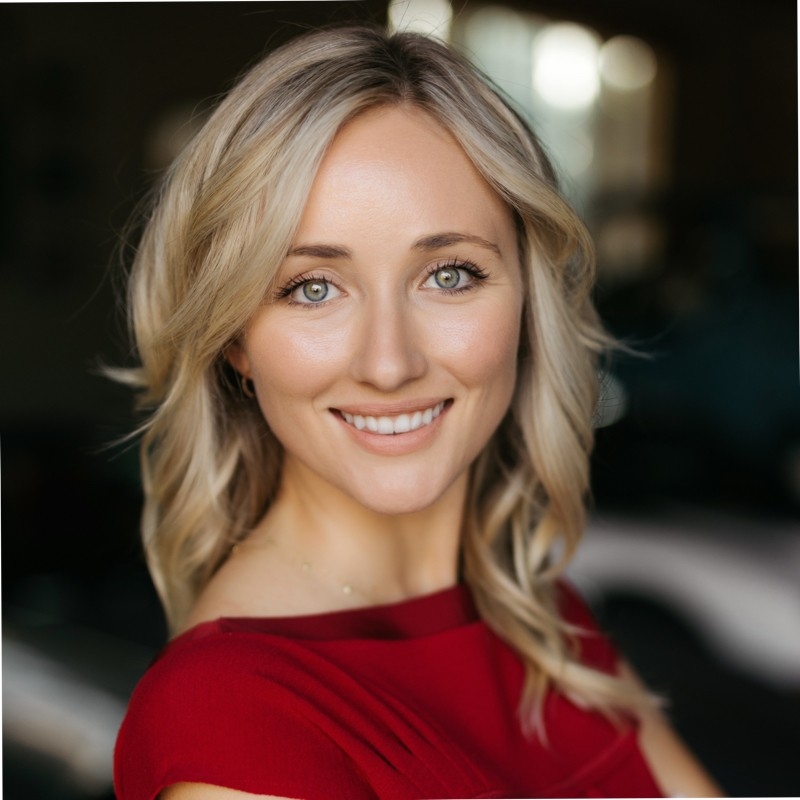 Headshot of a blond woman, wearing a red dress, smiling at the camera