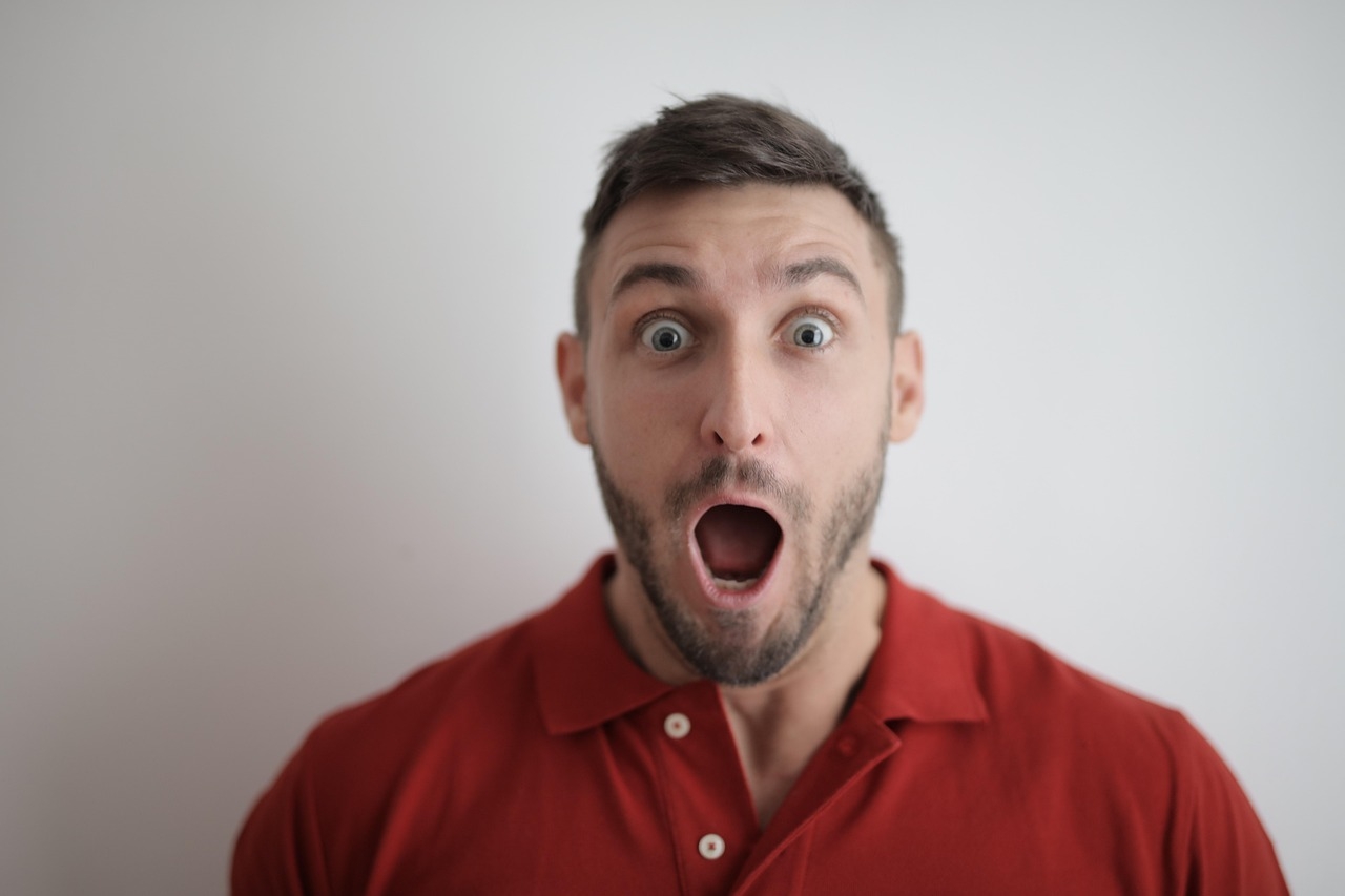 photo of a man, wearing a red shirt, with a shocked expression on his face.