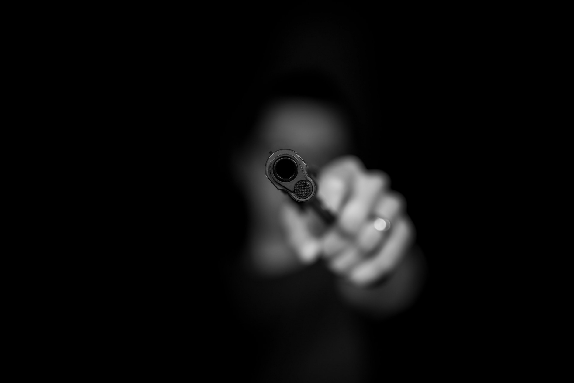 grayscale photo of a blurry person pointing a pistol at the viewer