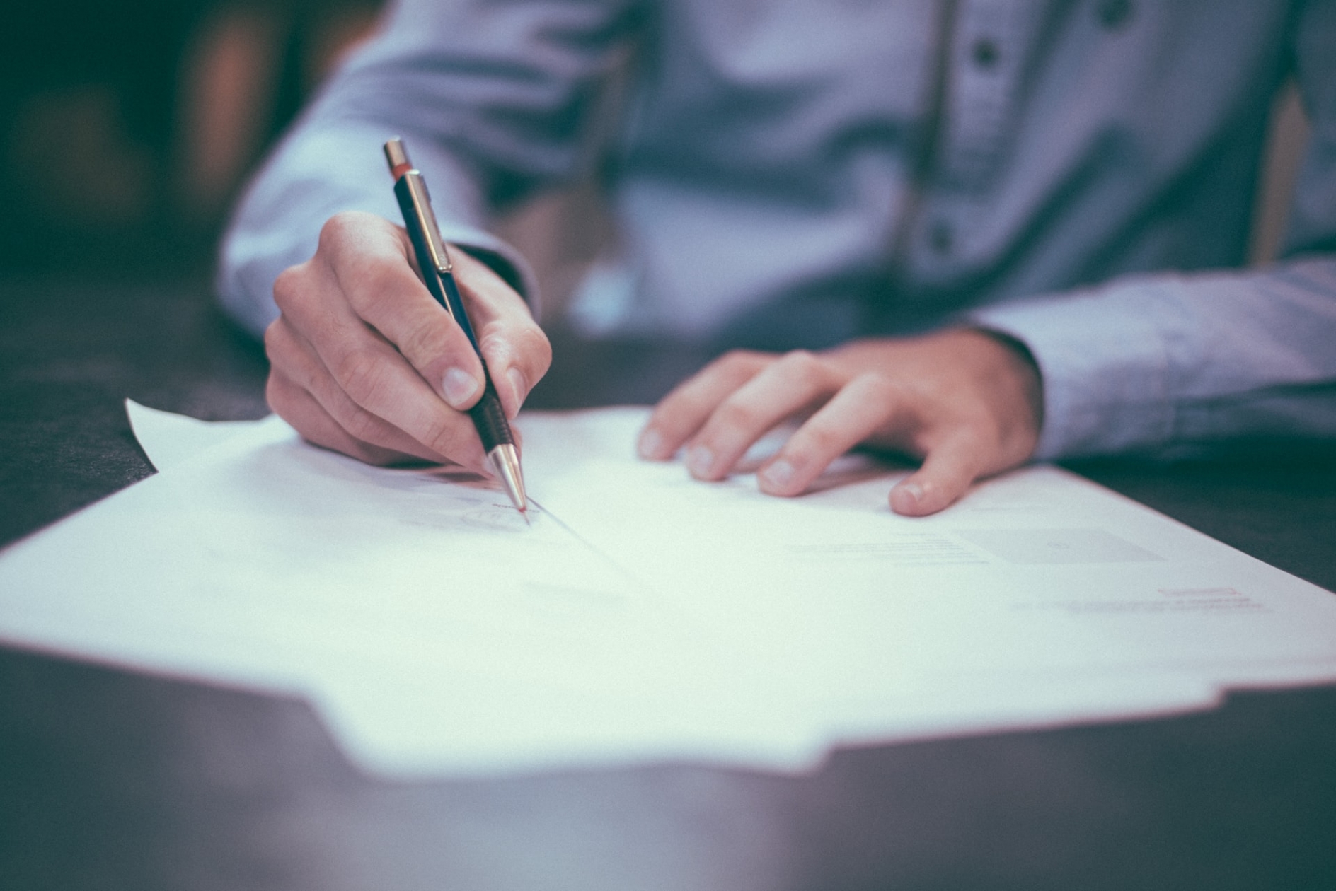 Man, sitting at a table, signing a stack of papers
