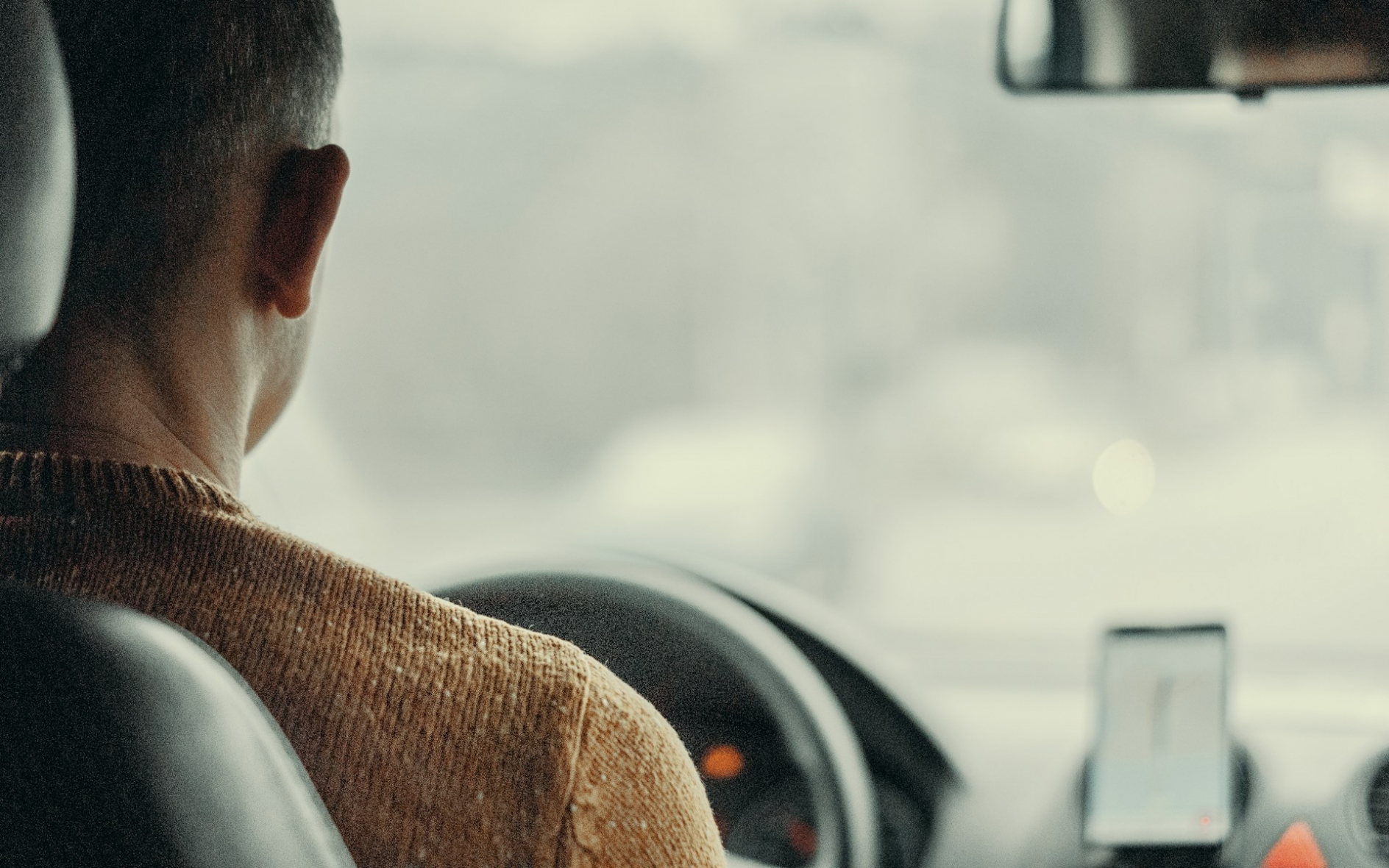 view from the back seat of a man driving a car, with his phone visible on the dashboard, displaying a map