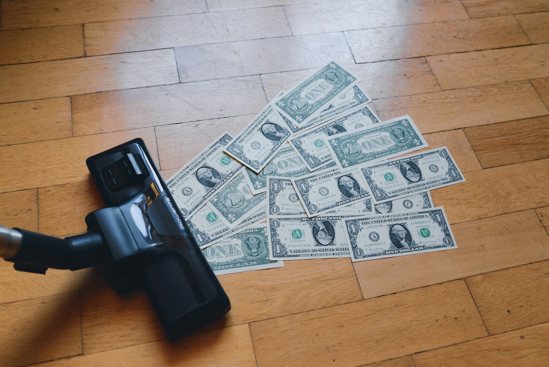 A vacuum cleaner sucking up a pile of money sitting on top of a wooden floor