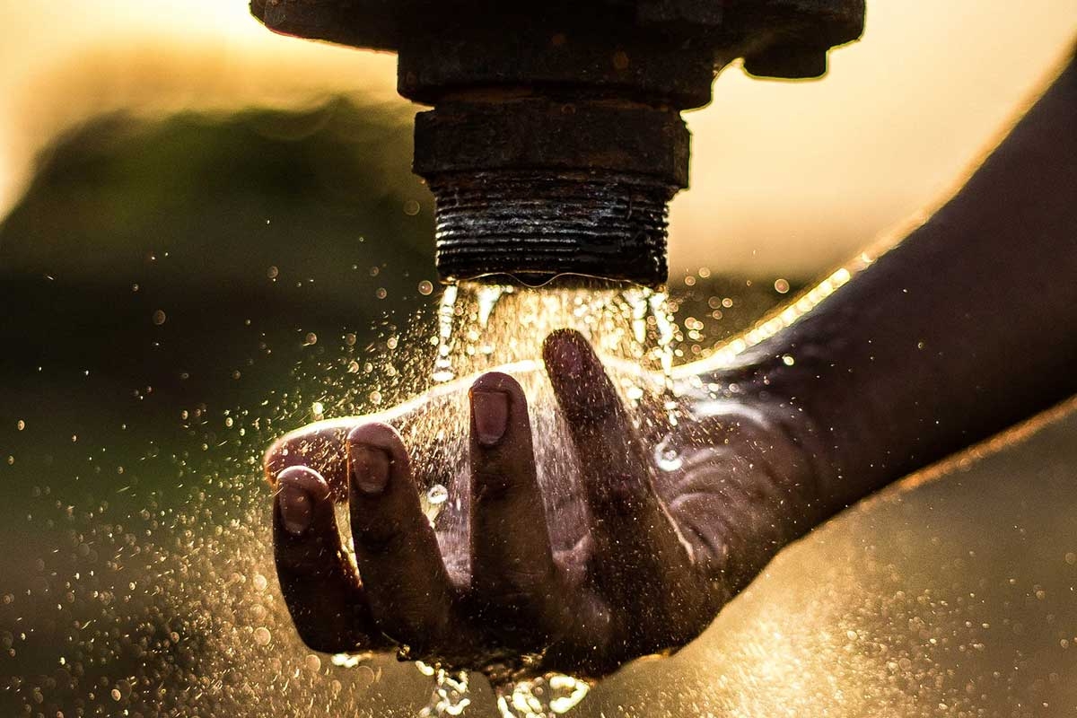 A dark-skinned hand, catching water that's pouring out of a pipe