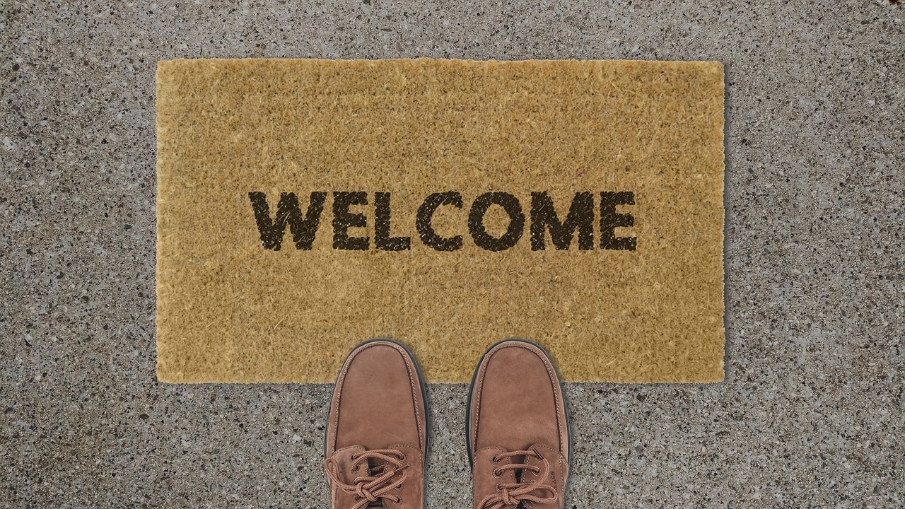 Two shoes standing at a doormat with the word WELCOME printed on it