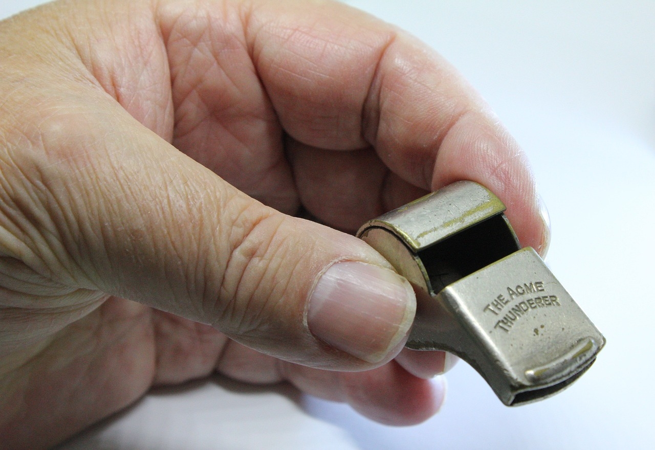A man's hand, holding a metal whistle