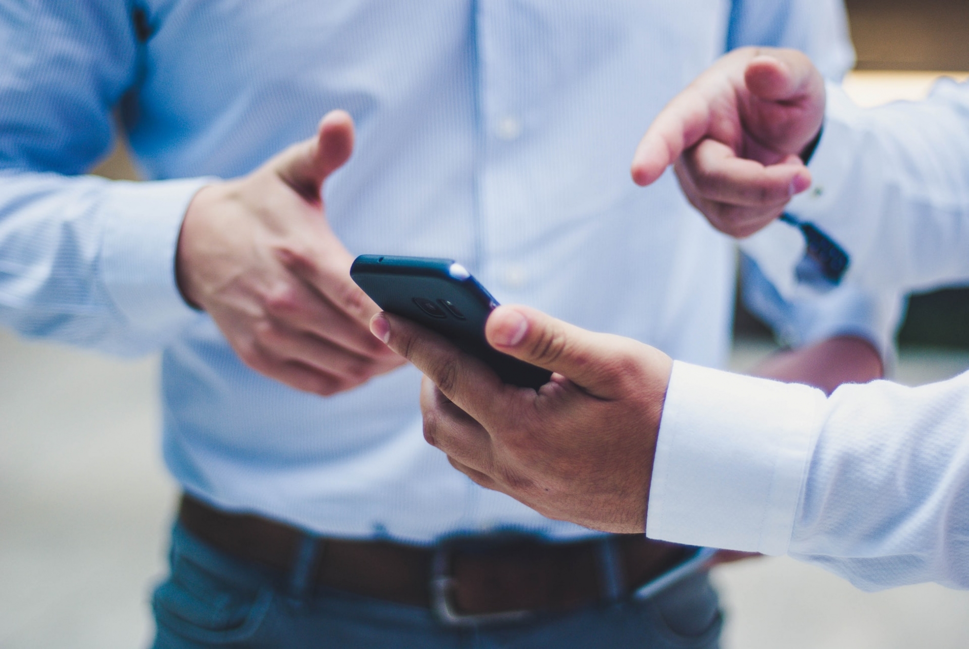 Man holding a smartphone and pointing at the screen, while talking to a second man