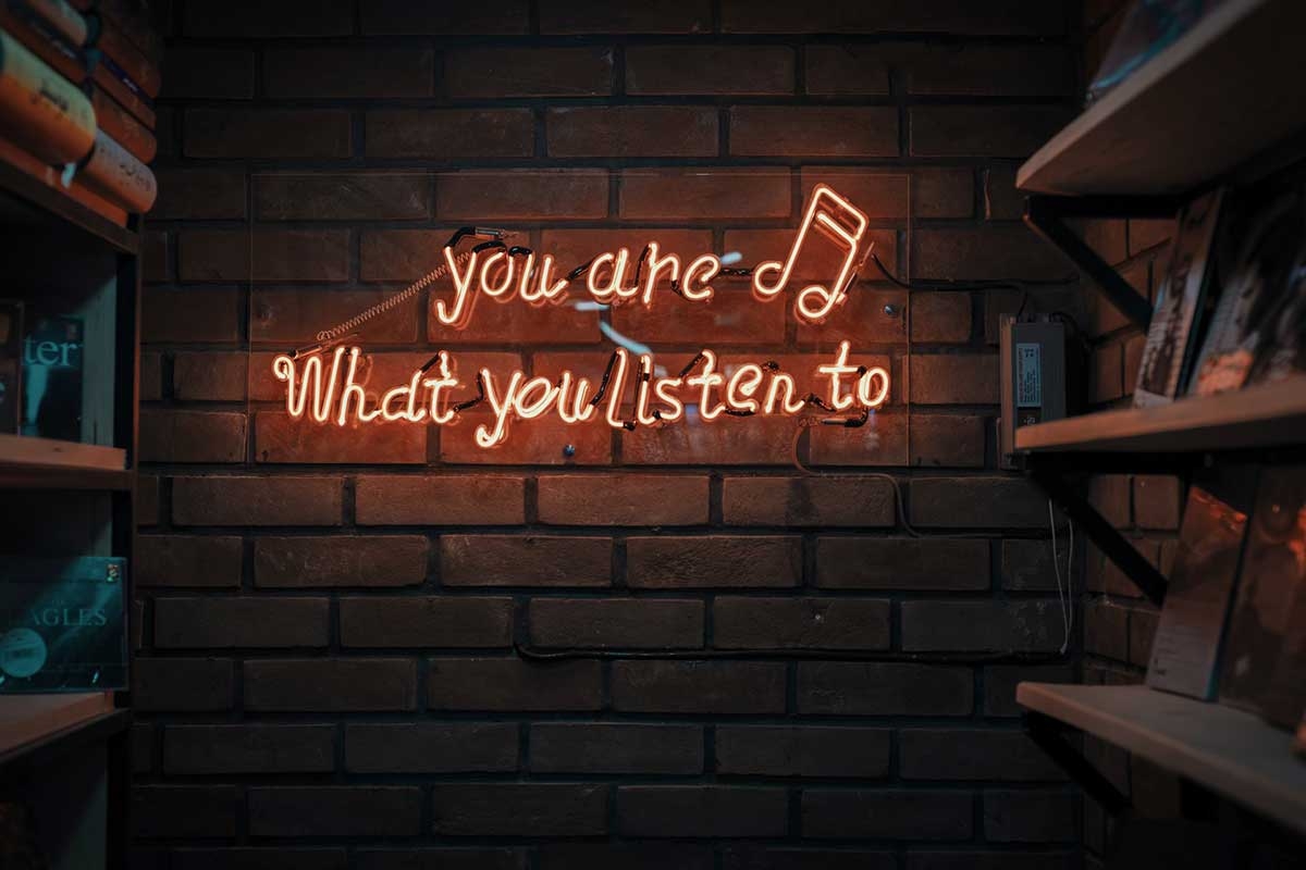 A neon sign on a brick wall that reads you are what you listen to